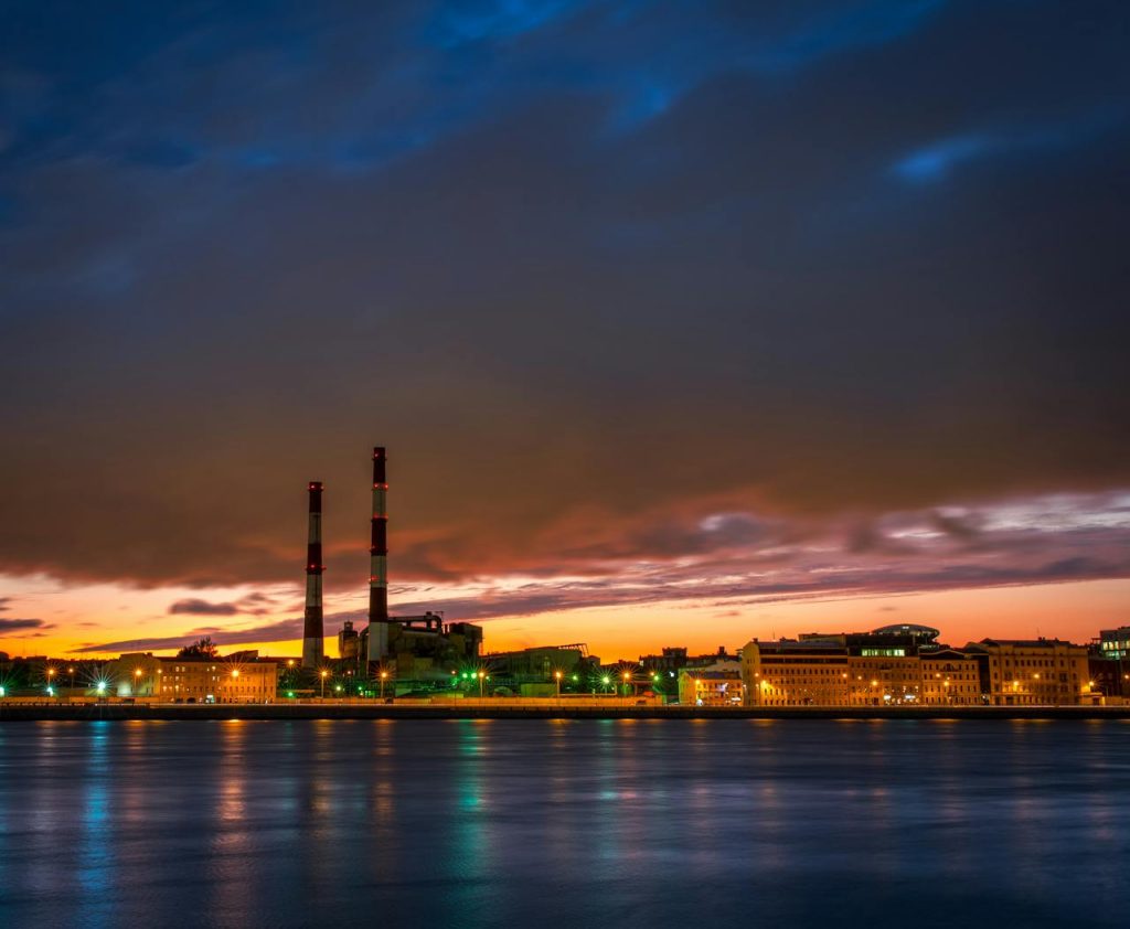 industrial cyber security cityscape reflecting on water during sunset, showcasing urban lights and clouds.